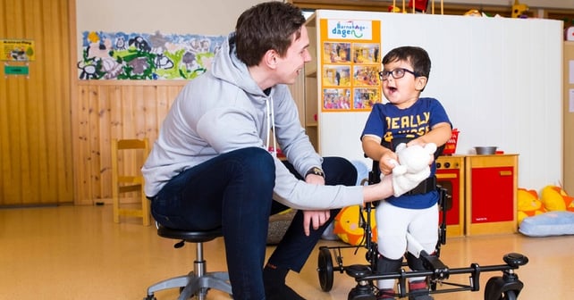 Physiotherapist and a boy with disability in a gait trainer