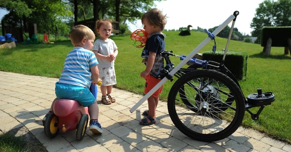Small children playing in the park, one in a Hibbot assitive device