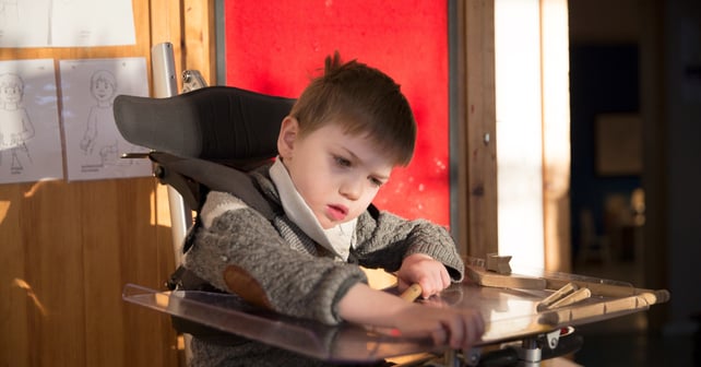 Boy with disability sitting in assitive device. 