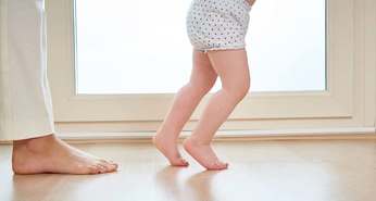 Young child walking with assistant from adult